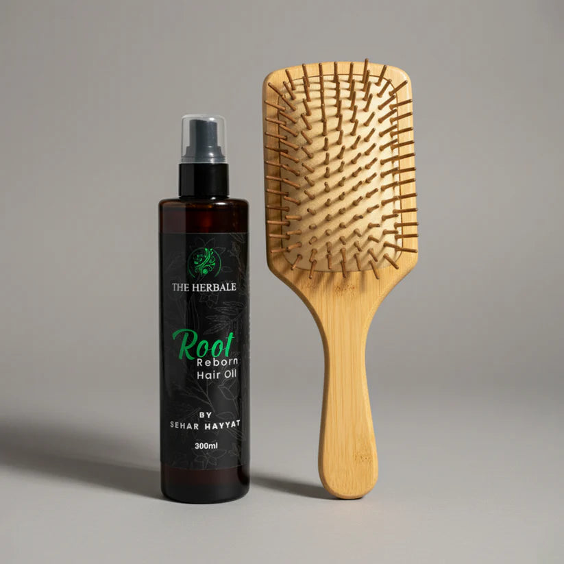 The Herbale Root Reborn Hair Oil 300ml bottle alongside a wooden paddle hairbrush on a beige background.