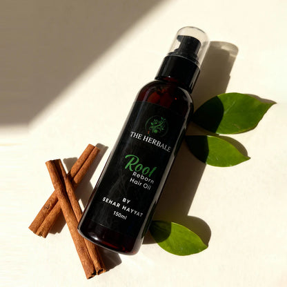 Root Reborn Hair Oil by Sehar Hayvat - 150ml bottle with cinnamon sticks and fresh green leaves, placed in natural light, offering a rejuvenating hair care solution for nourishment and strength.