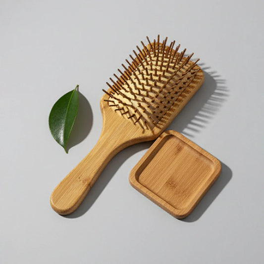 Wooden paddle hairbrush placed beside a small wooden tray and a green leaf, emphasizing natural hair care products.